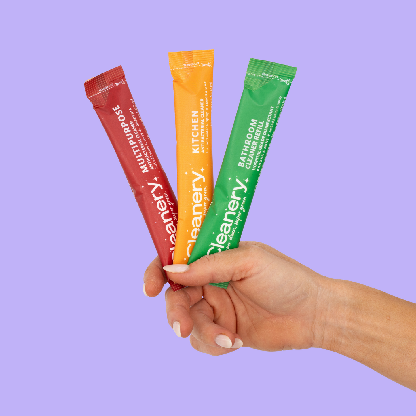 Hand holding three colorful 'Cleanery' cleaning stick packs against a purple background