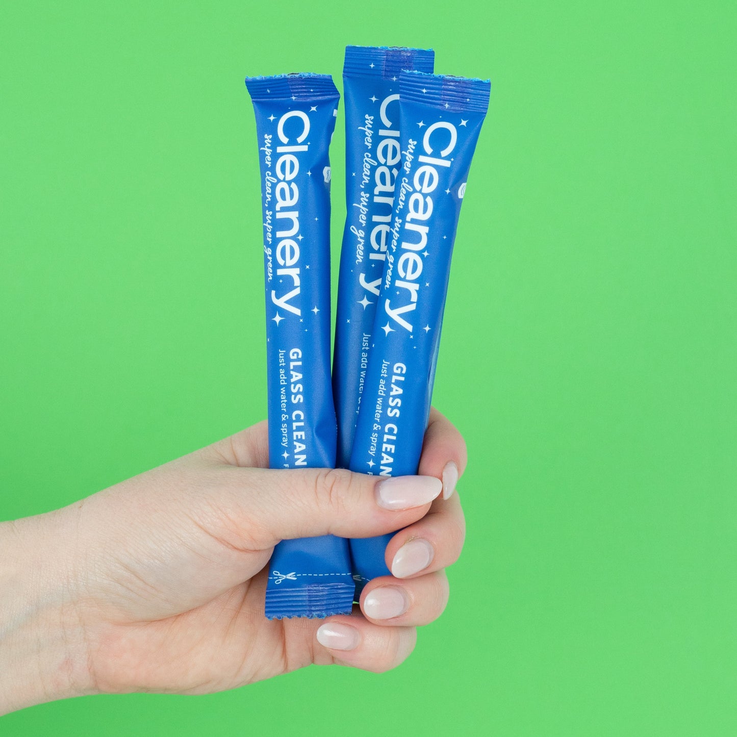 Hand holding four blue Cleanery glass cleaner refills against a green background
