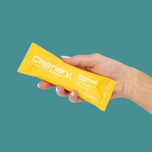 Hand holding a yellow Cleanery product package against a teal background