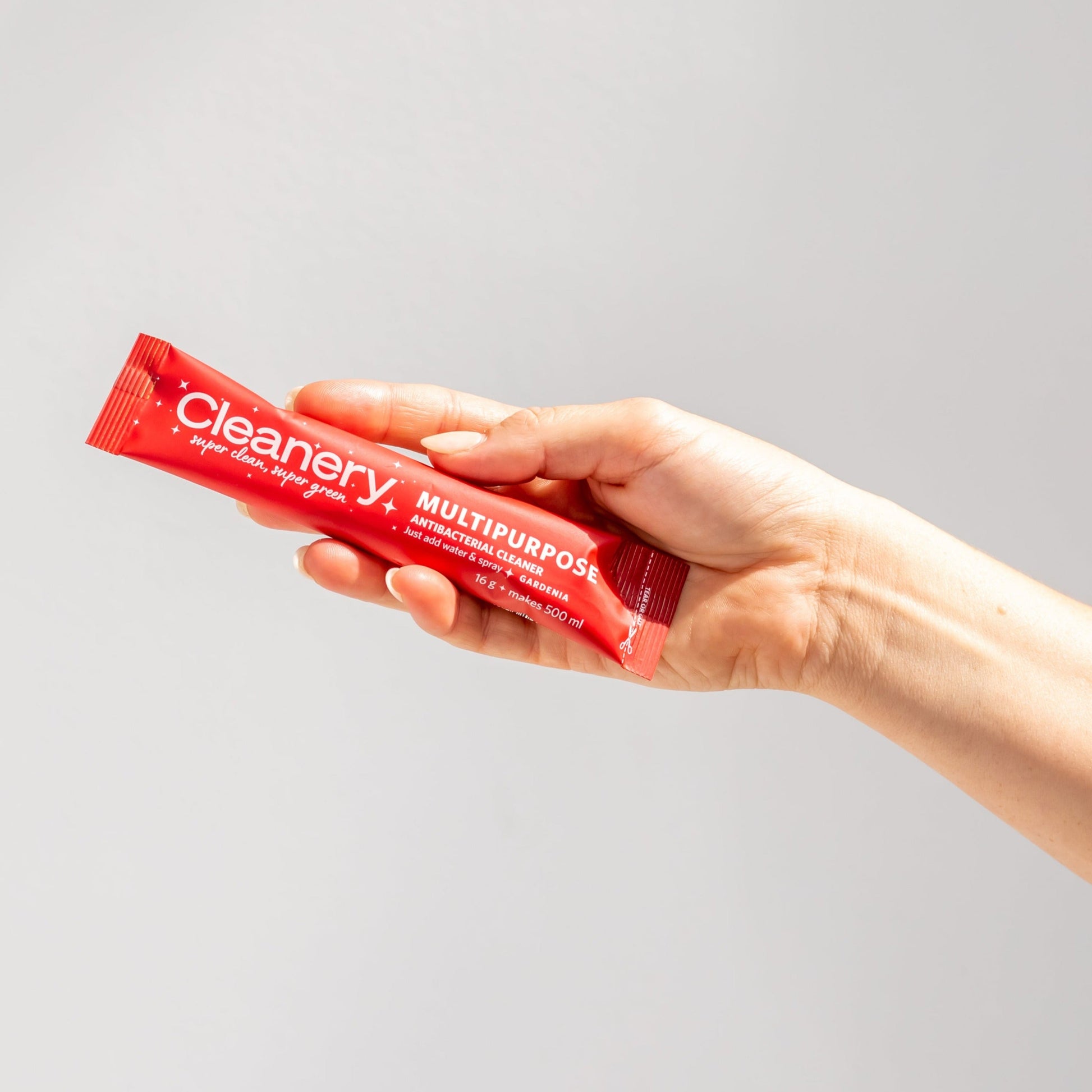 A hand holding a red sachet of multipurpose cleaning spray with the brand 'Cleanery' visible on the packaging.