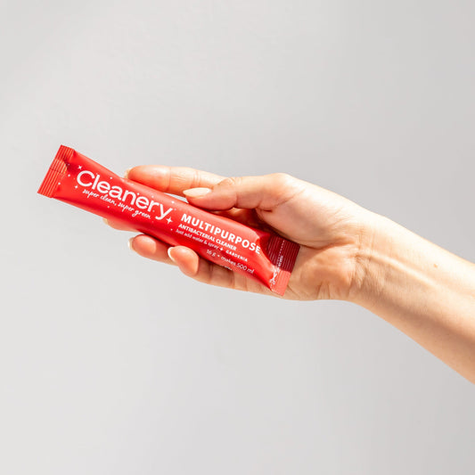 A hand holding a red sachet of multipurpose cleaning spray with the brand 'Cleanery' visible on the packaging.