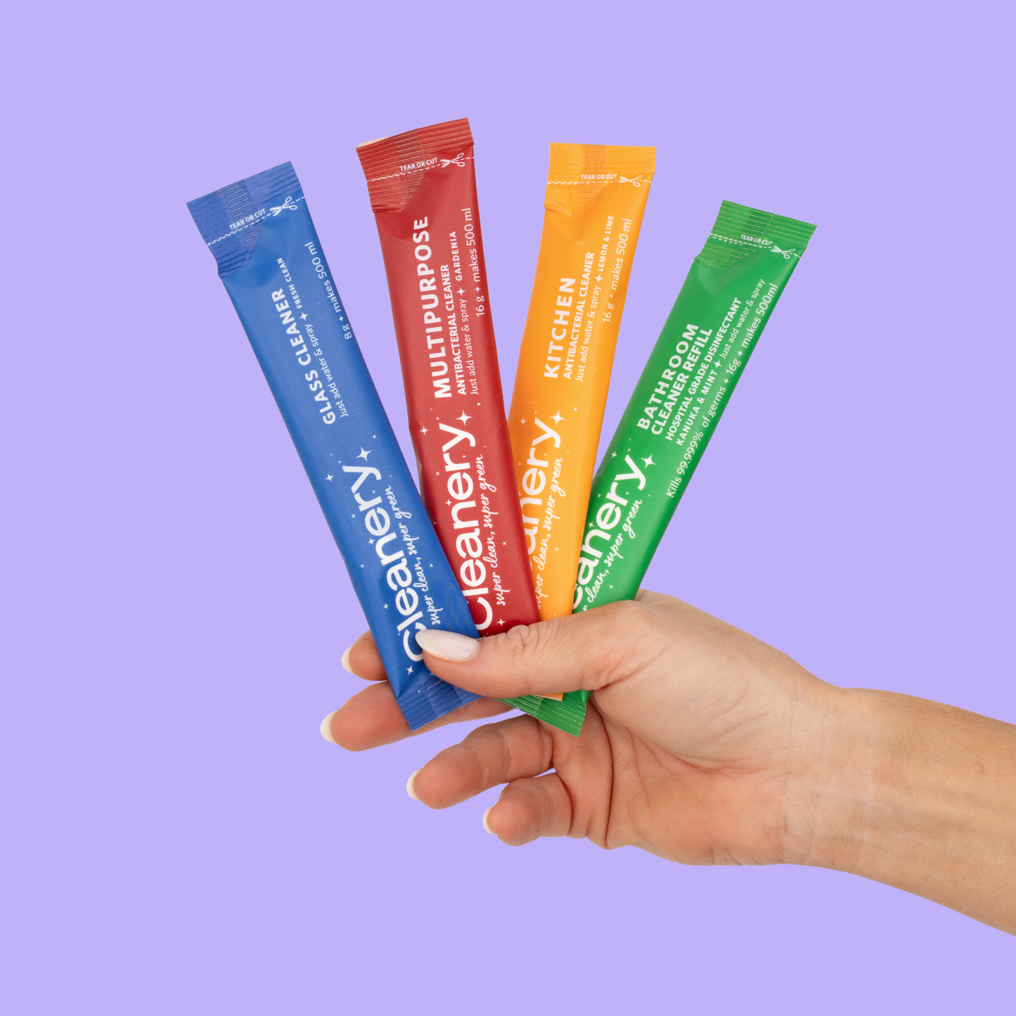 Hand holding four colorful packets of Cleanery cleaning products against a purple background