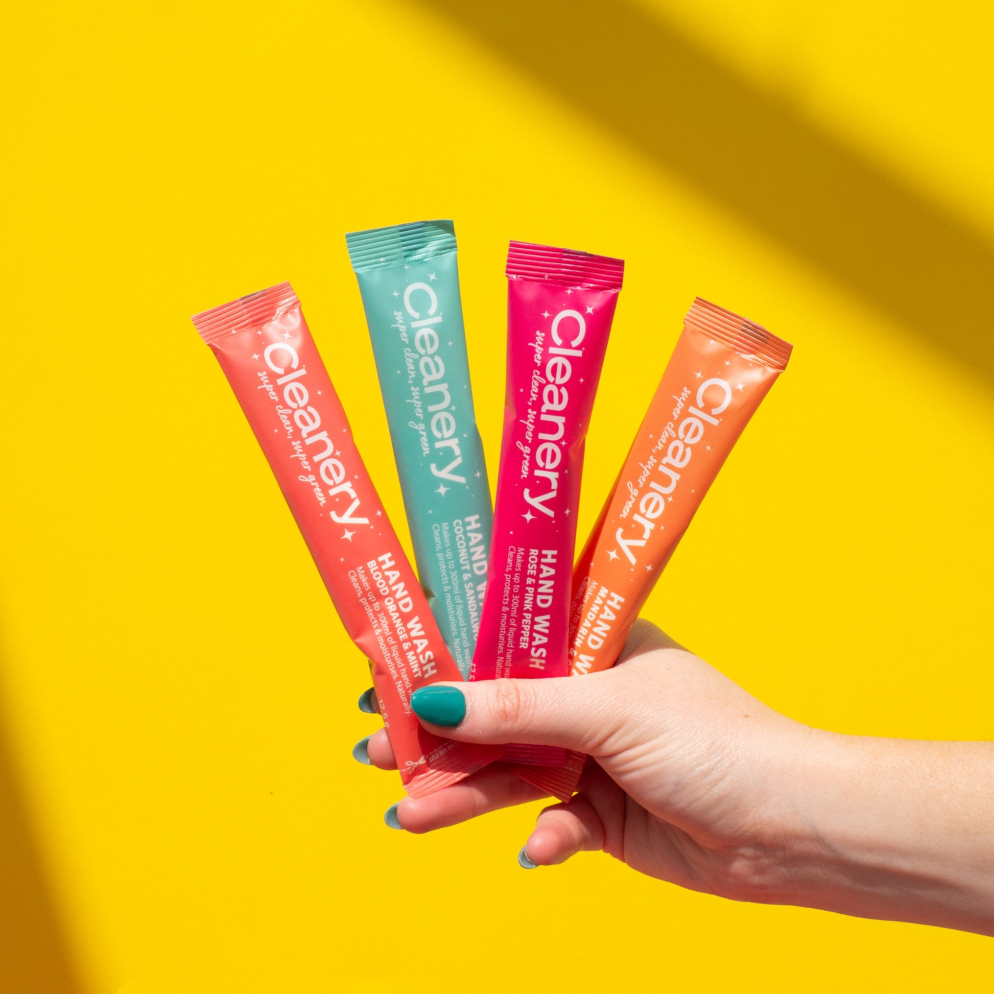 Hand holding four Cleanery refills sachets against a yellow background