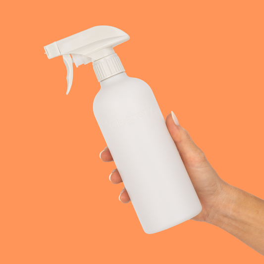 White Cleanery reusable spray bottle held by a hand against an orange background