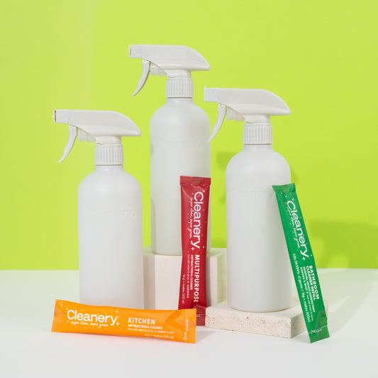 Three white spray bottles and three refills of Cleanery products on a white surface with a green background