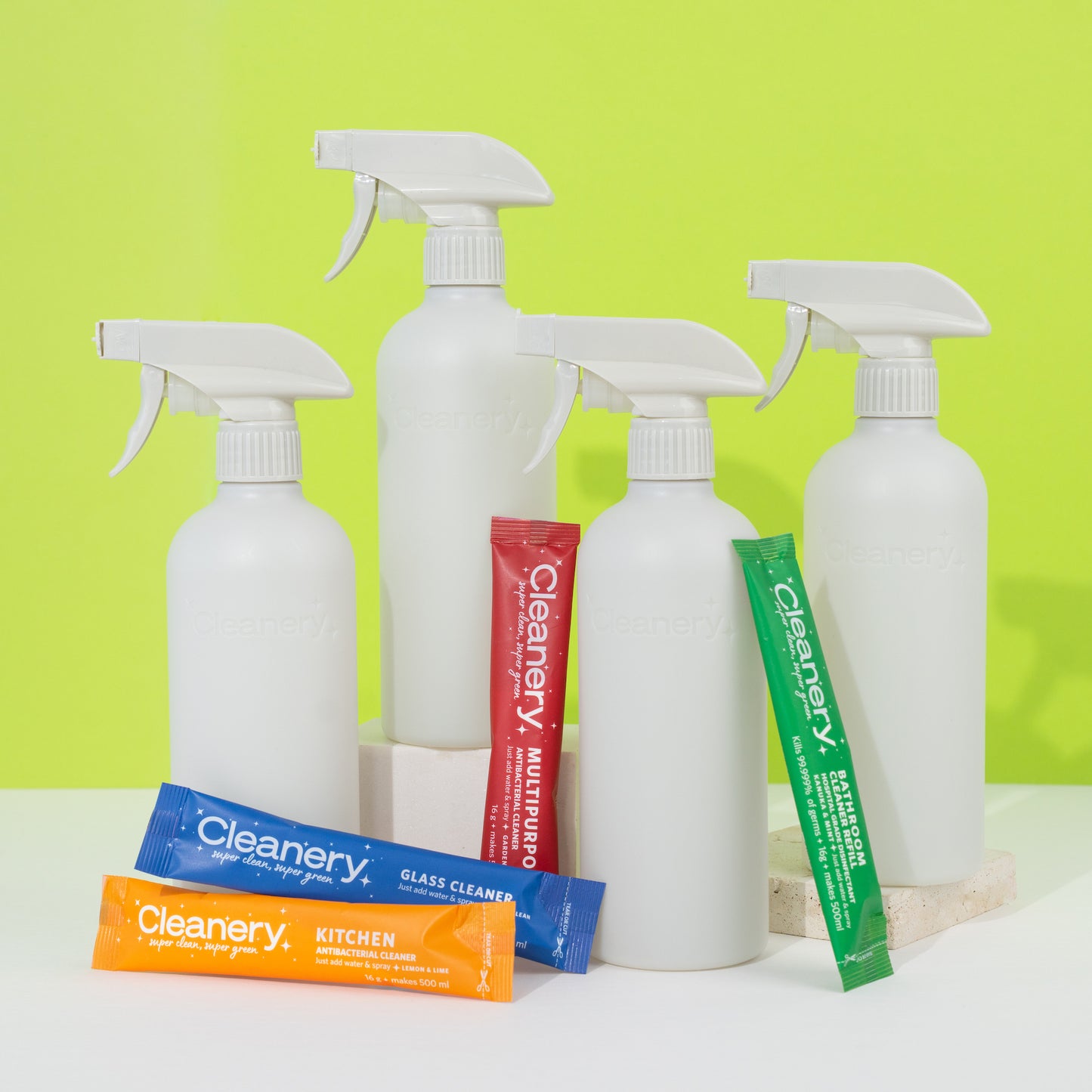 White Cleanery spray bottles and colorful packaging on a white surface with a green background