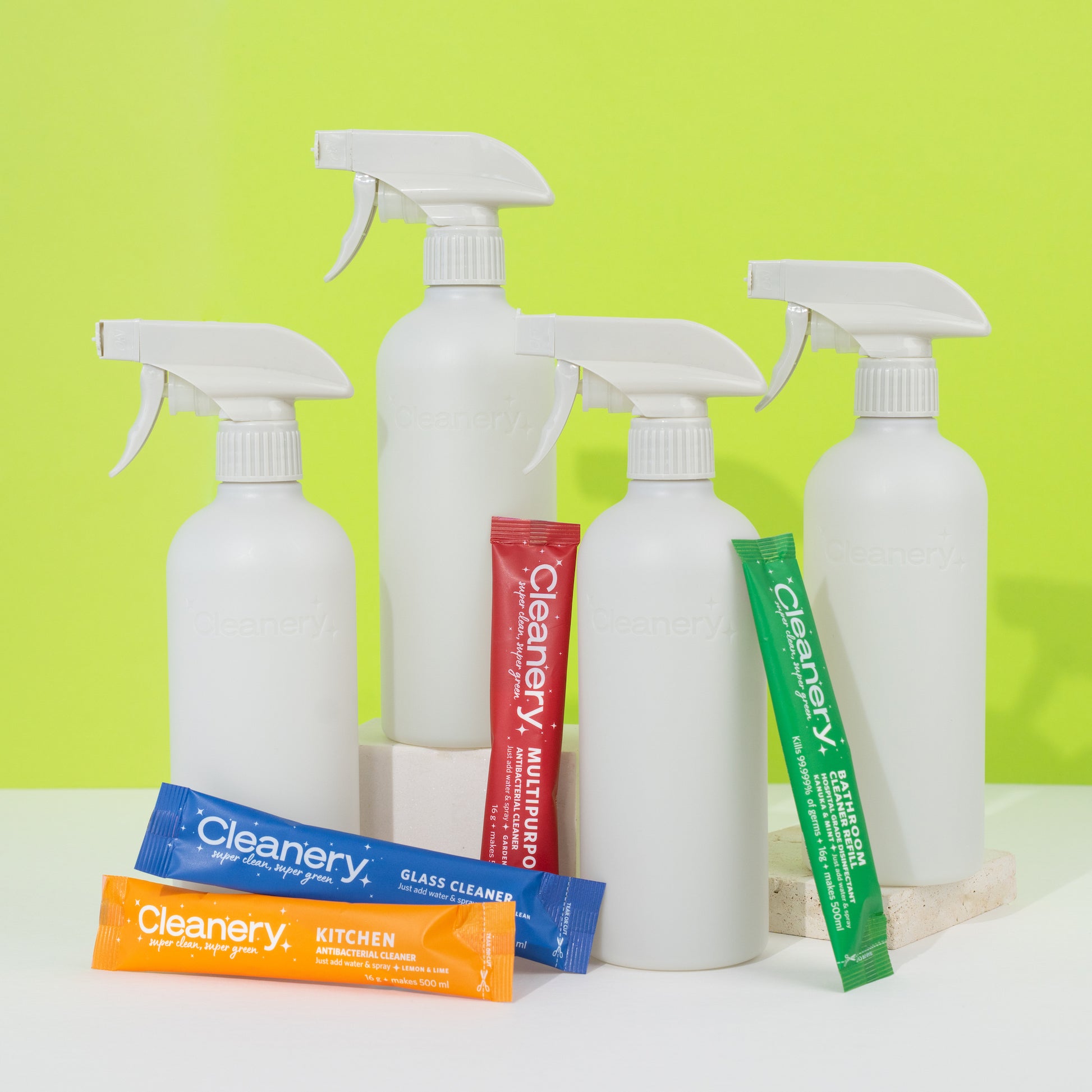 White Cleanery spray bottles and colorful packaging on a white surface with a green background
