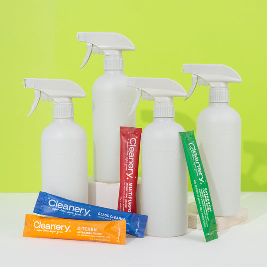 White Cleanery spray bottles and colorful packaging on a white surface with a green background